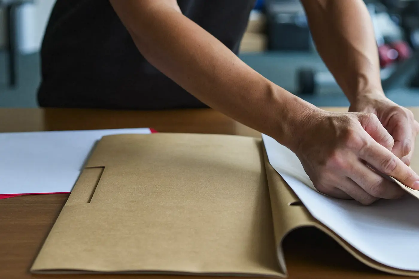 Mani che appoggiano una cartellina chiusa su una scrivania di legno in palestra