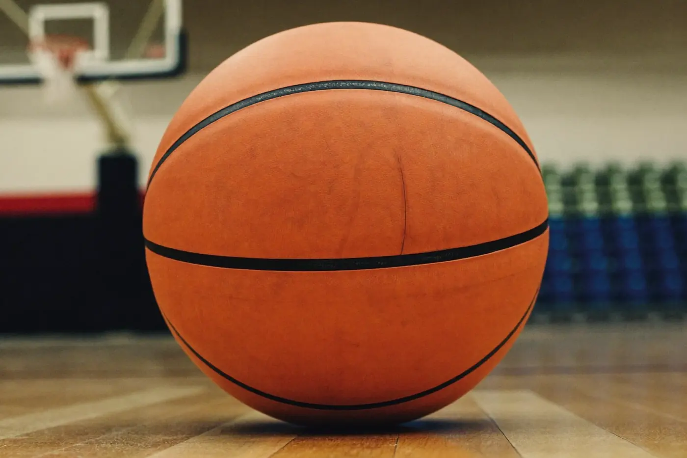 Pallone da basket appoggiato sul parquet in primo piano, squadra di ragazzi sfocata sullo sfondo durante l'allenamento