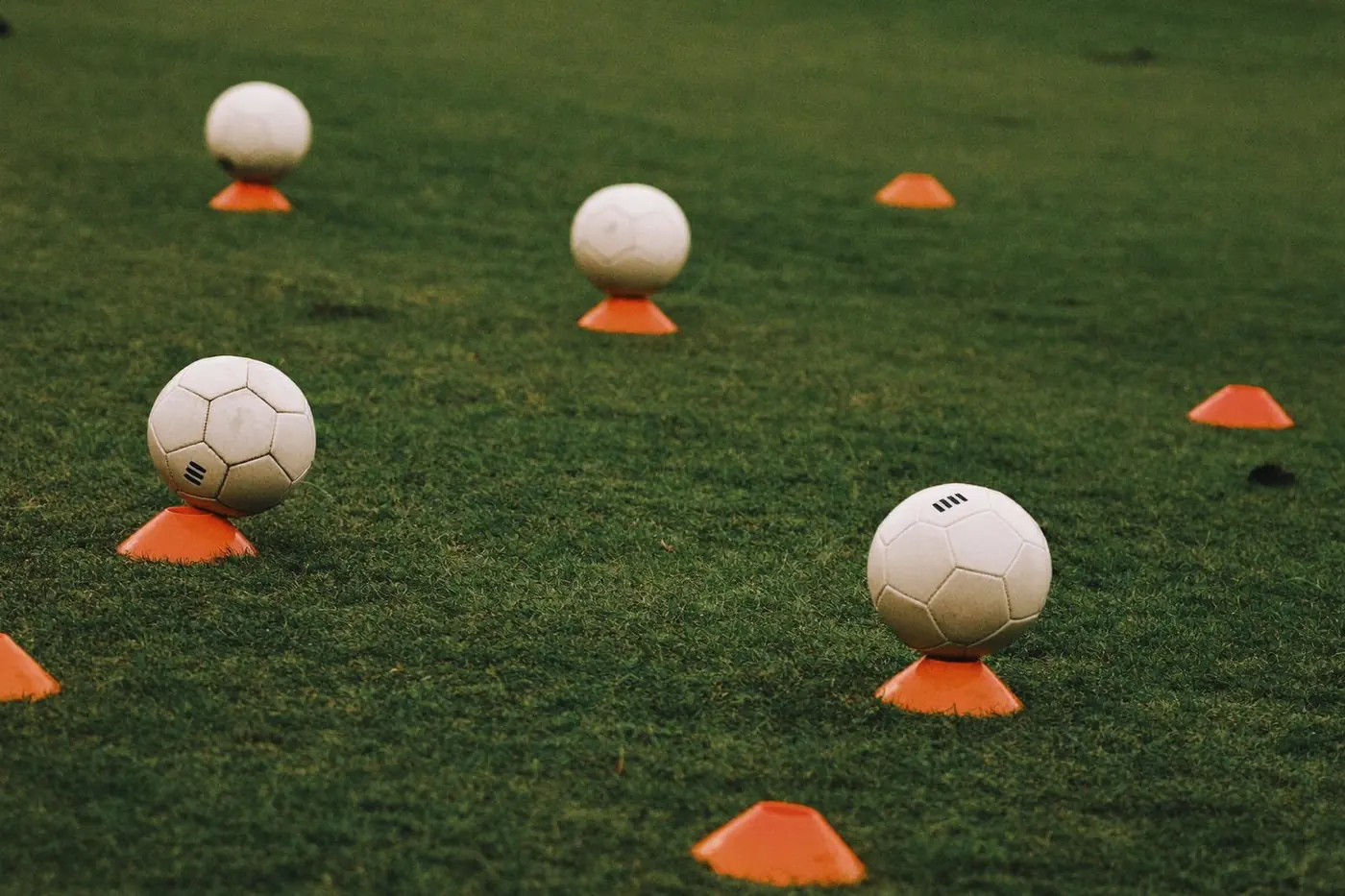 Coni e palloni disposti su un campo in erba prima di un allenamento di calcio giovanile