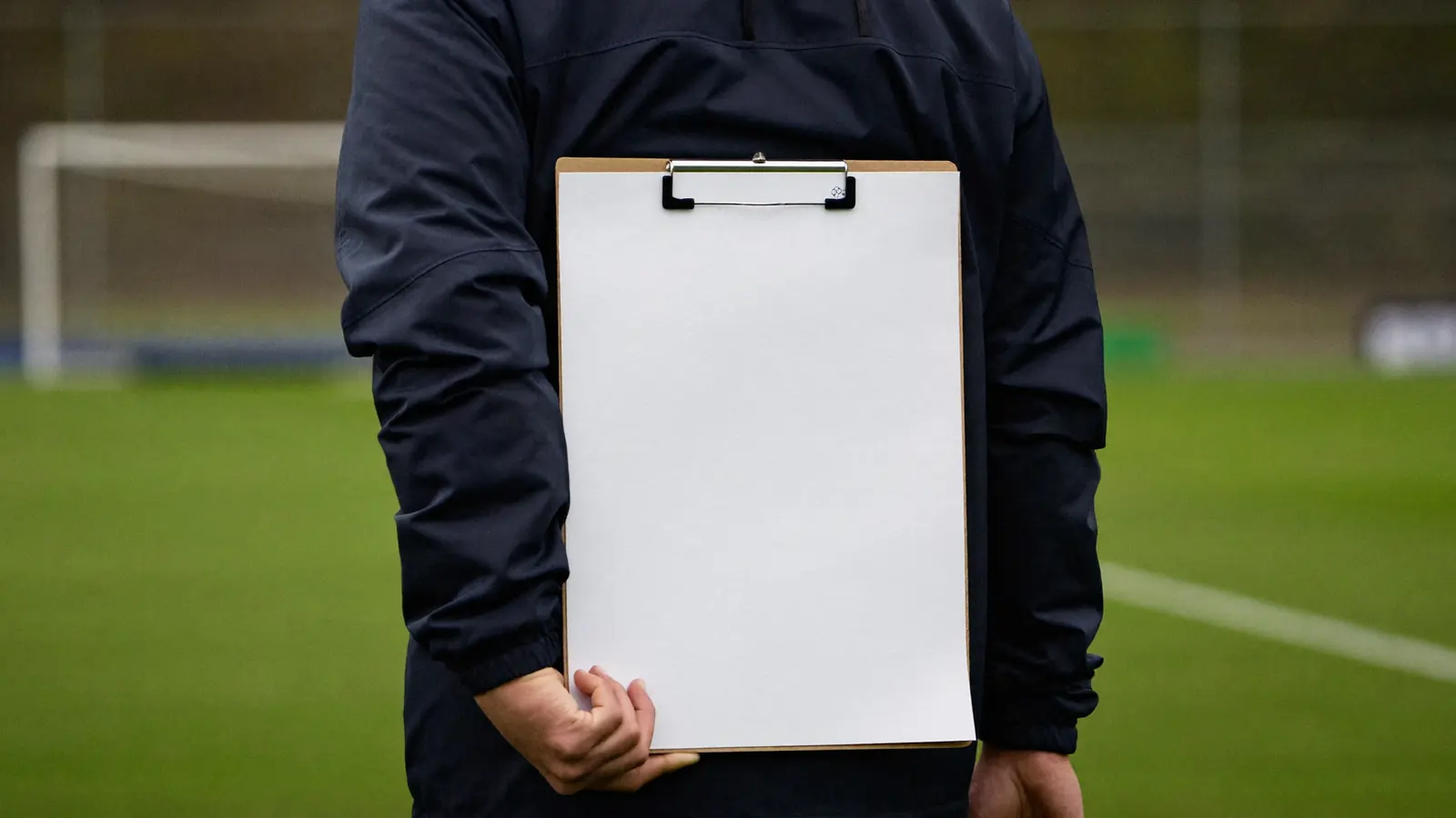 Allenatore di calcio giovanile di spalle a bordo campo con una cartellina in mano