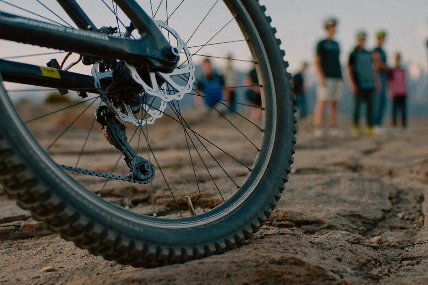 Dettaglio della ruota di una mountain bike su un sentiero sassoso con il gruppo sfocato sullo sfondo