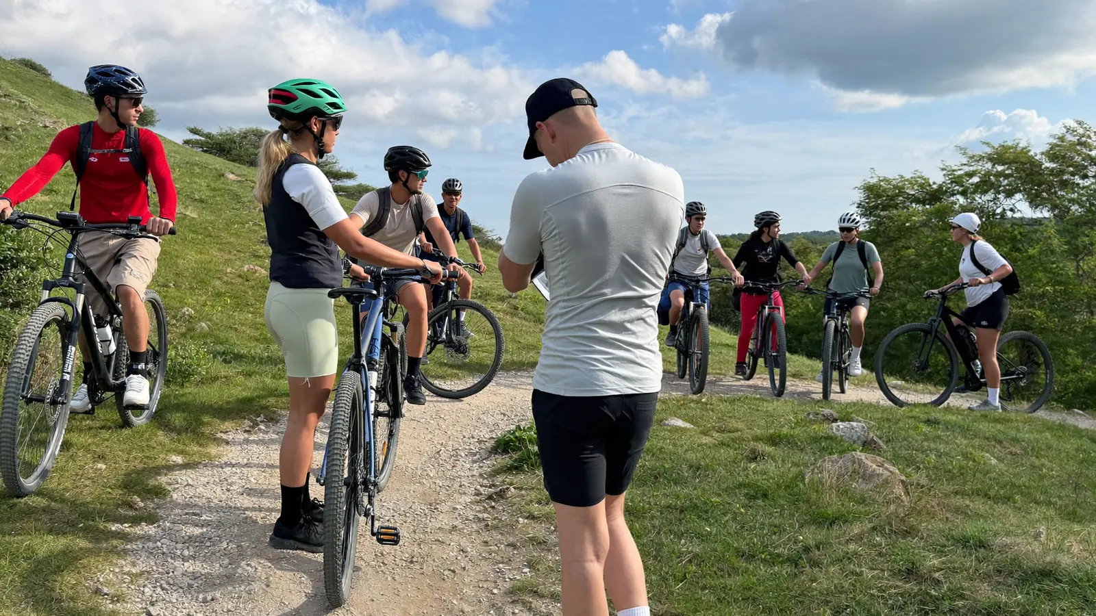 Gruppo di adulti in mountain bike su uno sterrato collinare con una guida ferma davanti a loro che spiega il percorso al mattino