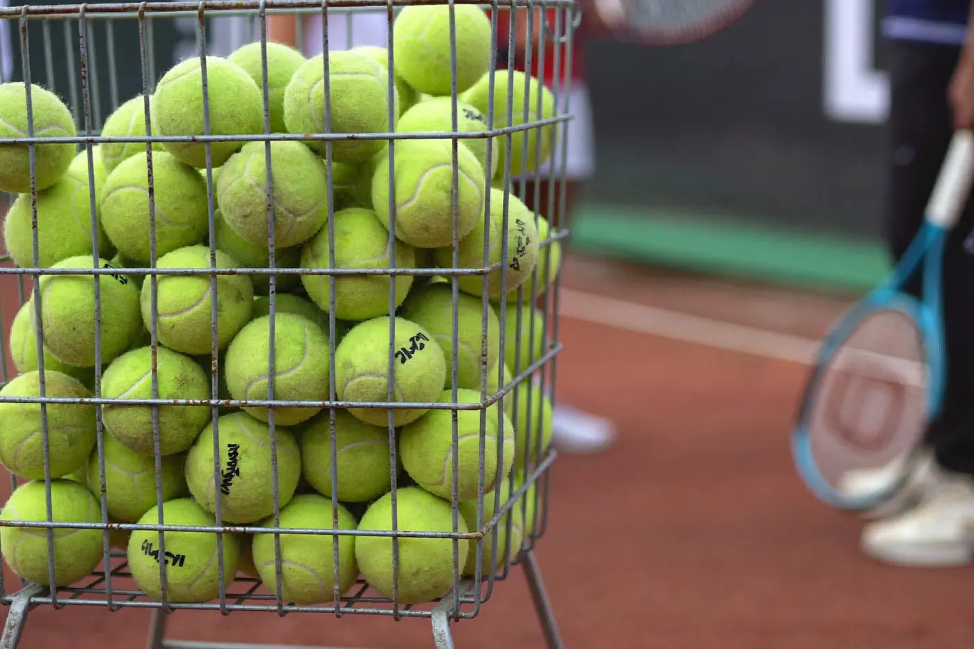 Cesto di palline da tennis a bordo campo con un piccolo gruppo di adulti che ascolta la spiegazione dell'istruttore