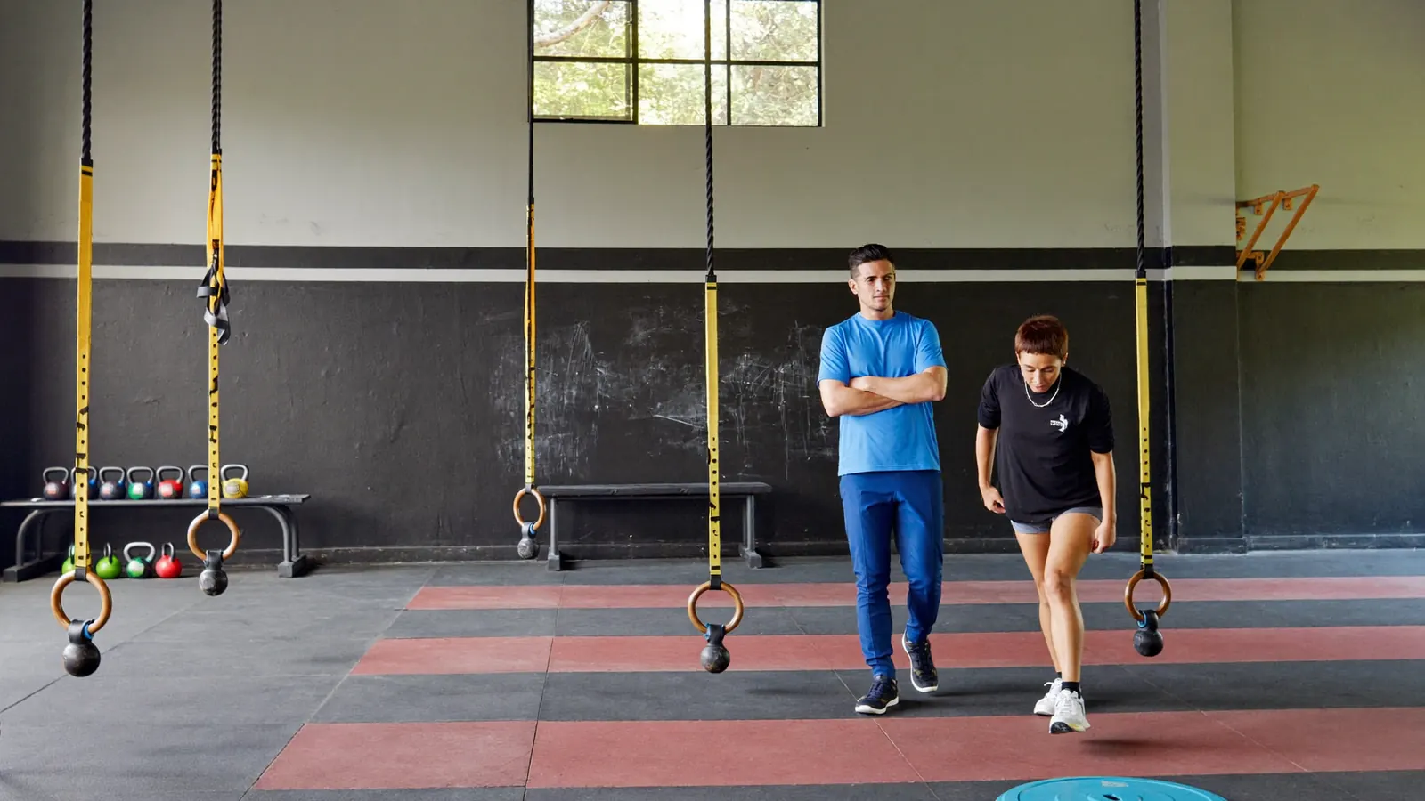 Coach segue un cliente adulto in un'area functional con kettlebell e corde