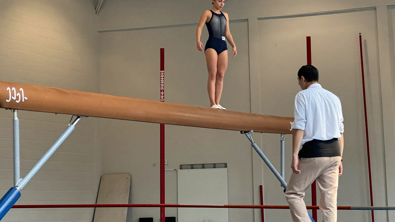 Tecnico assiste una ginnasta sulla trave in una palestra di ginnastica artistica