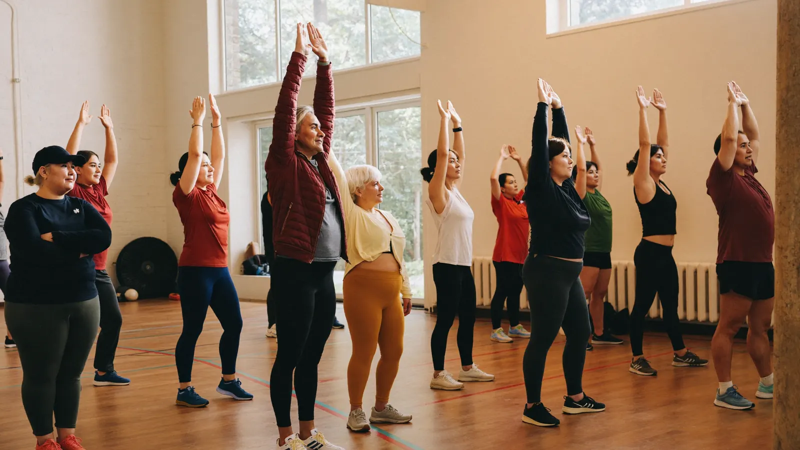 Gruppo di adulti esegue movimenti lenti di mobilita' guidati da un'istruttrice in una palestra luminosa