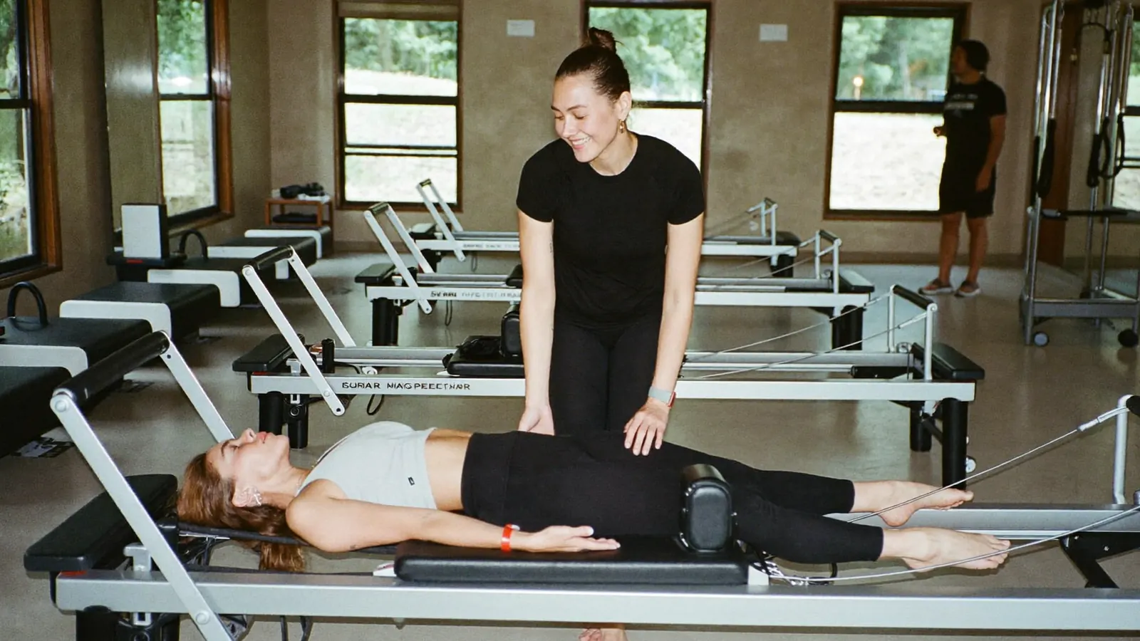 Istruttrice di pilates guida un allievo adulto sul reformer in uno studio luminoso