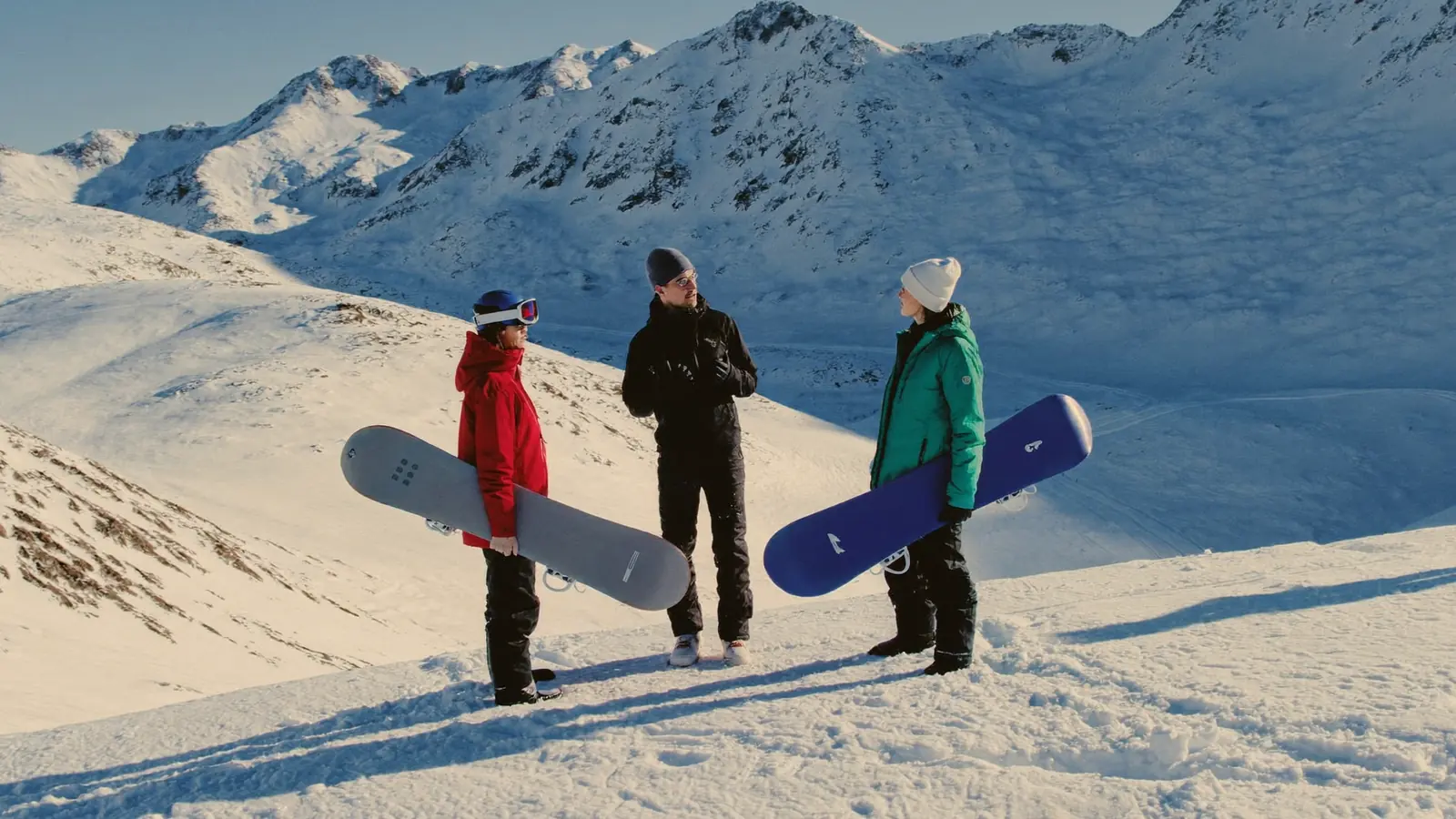 Maestro di snowboard spiega la tecnica a due allievi adulti con la tavola ai piedi su una pista innevata, montagne sullo sfondo