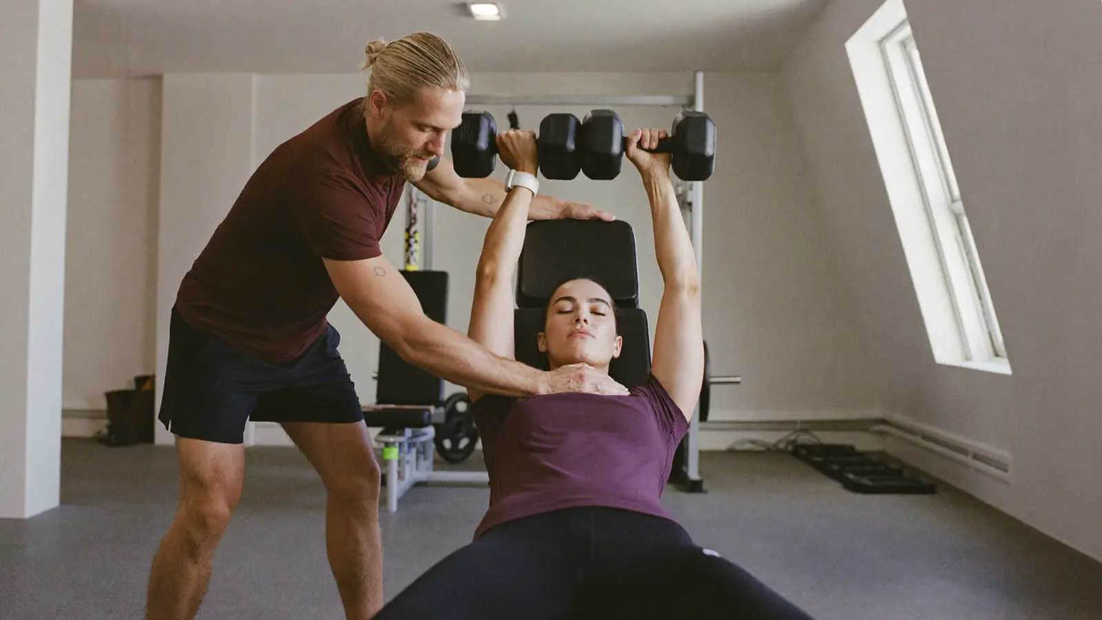 Personal trainer assiste una cliente durante una distensione con manubri