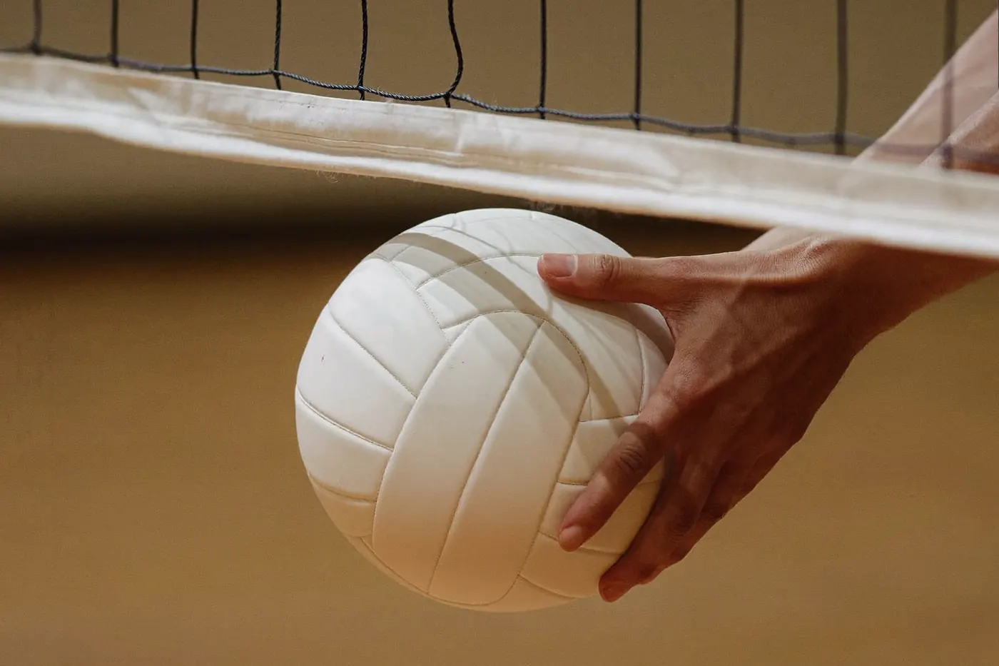 Carrello di palloni da pallavolo bianchi senza scritte accanto alla rete, parquet e luce calda