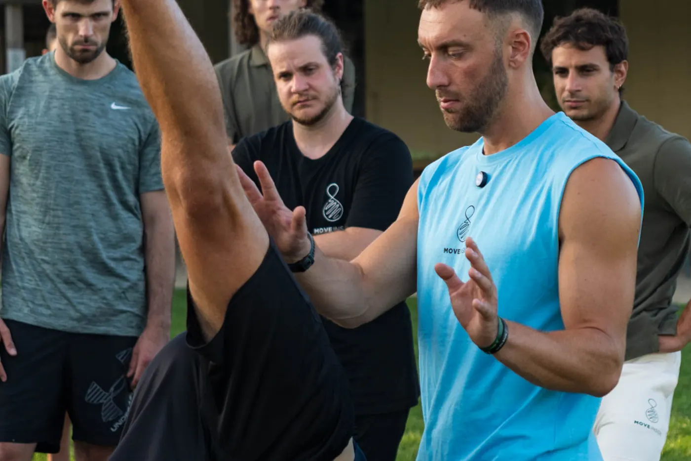 Coach che spiega un movimento con le mani a un gruppo di persone all'aperto, nella luce calda del pomeriggio